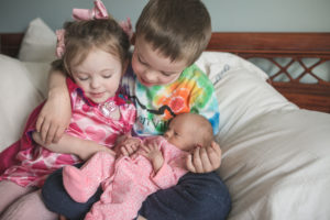 3 siblings 2 children holding baby